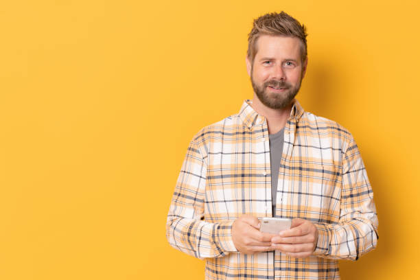 istock Young man in plaid shirt using smartphone isolated over yellow background. 1360038757