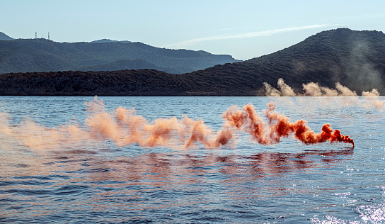 One orange colored smoke grenade in the blue sea. Distress call.