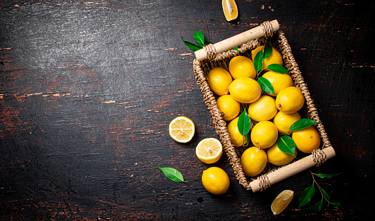 Fresh lemons with foliage in a basket. On a rustic dark background. High quality photo