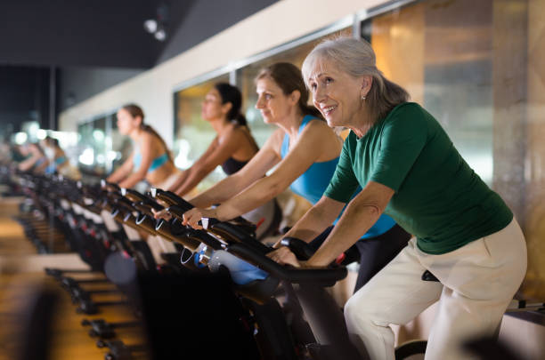 ältere frau, die sich im fitnessstudio auf dem fahrrad aufwärmt - aerobics stock-fotos und bilder