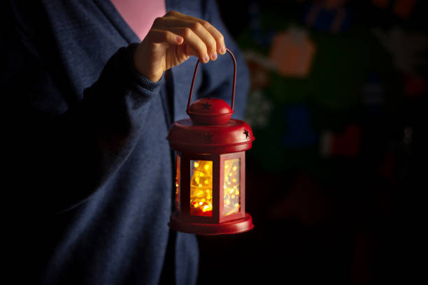 istock hand holds red christmas lantern in dark room. 1360042055