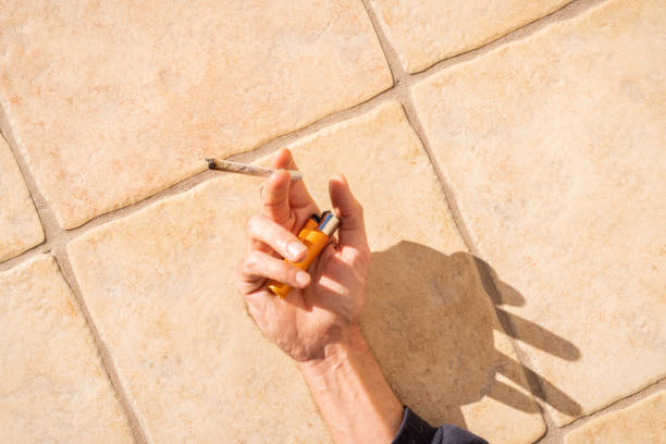 uma pessoa deitada ao sol segurando um baseado de maconha e um isqueiro. histórico de pessoas relaxando e fumando ao sol. - unrecognized person - fotografias e filmes do acervo