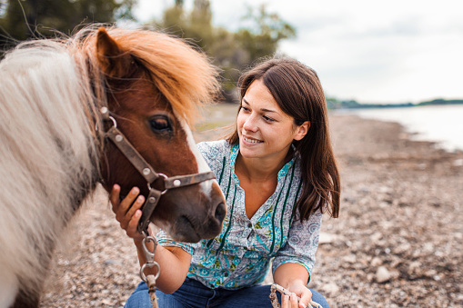 Portrait of a beautiful woman with her pony by the lake