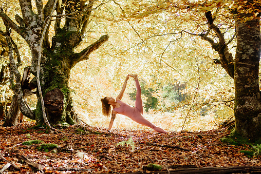 woman practicing yoga poses in a forest during fall.