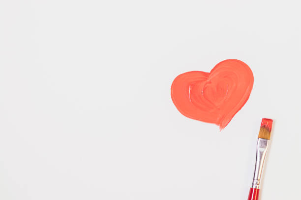 istock Heart drawn in red paint next to brush on white background 1360059069