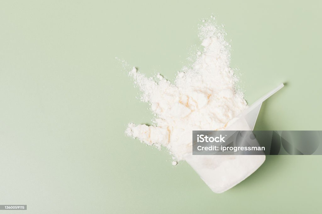 Whey protein powder sports nutrition scattered from measuring Whey protein powder sports nutrition scattered from measuring spoon on green background, flat lay Ground - Culinary Stock Photo