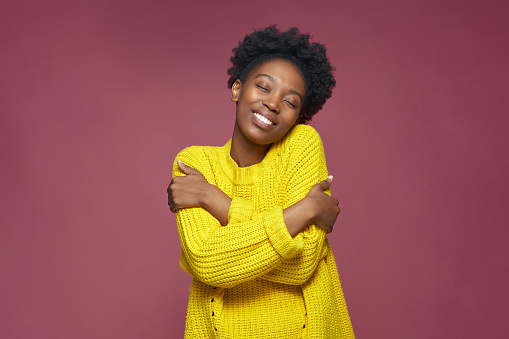 Love yourself, self acceptance. Smiling young african american woman embrace herself, closed eyes. Self-care concept. High quality photo