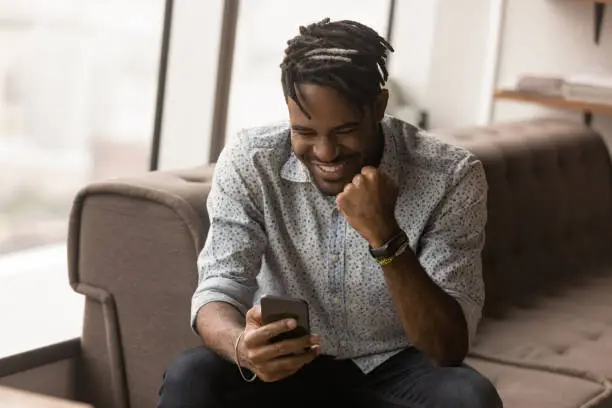 Photo of African guy read great news on smartphone feels overjoyed