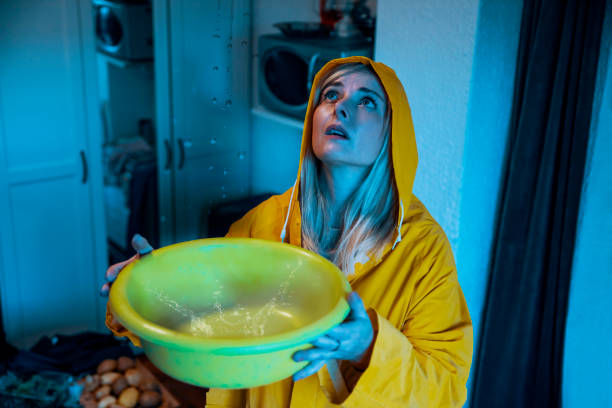 Rain storm at home in the middle of the night Woman in yellow raincoat collecting Water Leak From the Ceiling. A roof leak at night during the storm. Catching leaking water drop splash to a pot property damage stock pictures, royalty-free photos & images