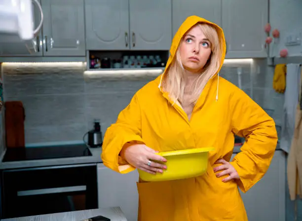 Worried Woman in yellow raincoat in  Home flooded by roof damage or broken pipe