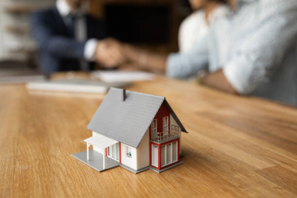 istock Miniature house on table, happy clients and Real Estate Agent on background 1360062797