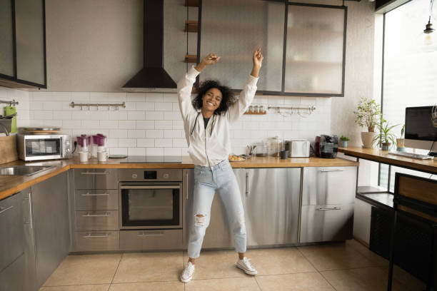 carefree african woman dancing in kitchen at home - extatisch stockfoto's en -beelden