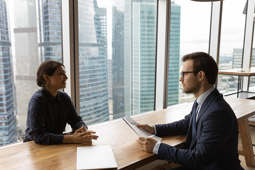 Multi ethnic business people negotiating in modern office. Indian female applicant take part in job interview answers questions talk to company HR manager Caucasian male in suit. Employment concept