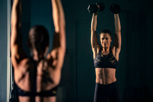 istock A young female doing exercise with a two dumbbell in front of a mirror 1360063400