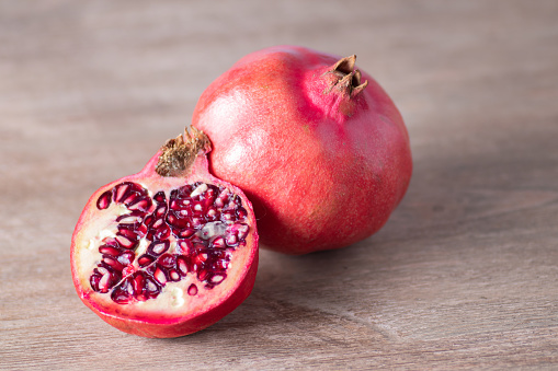Ripe and juicy pomegranate fruits, one whole and one cut in to quarter piece composition on kitchen table.
