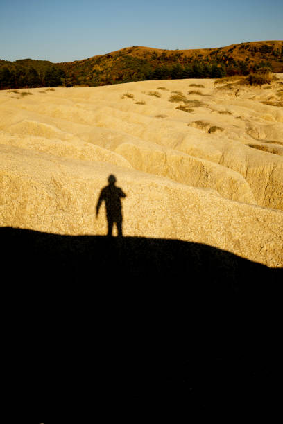 istock Man shadow silhouette (unrecognizable) projected over a dried mud ravine yellowed by the setting sun at Berca Mud Volcanoes reservation 1360064376