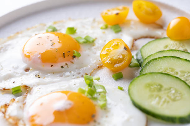 fried eggs vegetables on a white plate on a white wooden background.