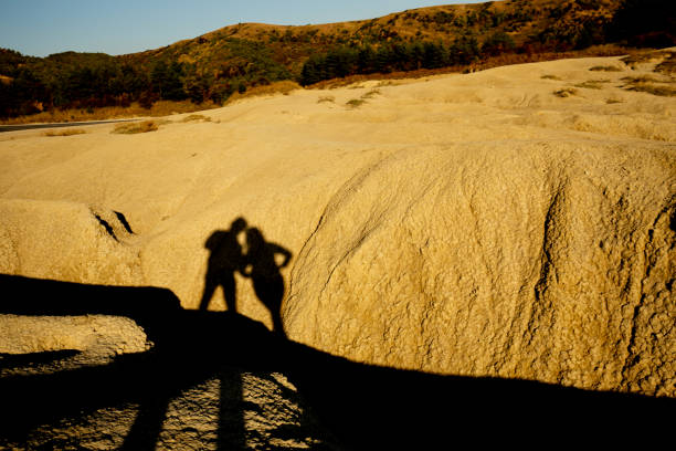 istock Man and woman shadow silhouettes projected over a dried mud ravine yellowed by the setting sun at Berca Mud Volcanoes reservation 1360068310