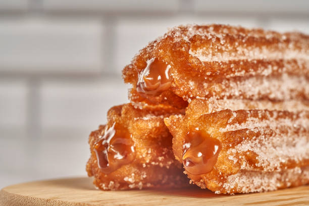 three churros filled with dulce de leche caramel on a wooden board three churros filled with dulce de leche caramel on a wooden board dulce de leche stock pictures, royalty-free photos & images