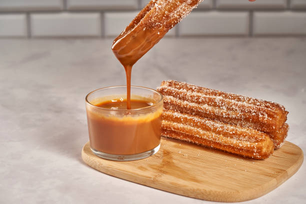 Dipping churro in dulce de leche caramel. Wooden board with churros Dipping churro in dulce de leche caramel. Wooden board with churros dulce de leche stock pictures, royalty-free photos & images