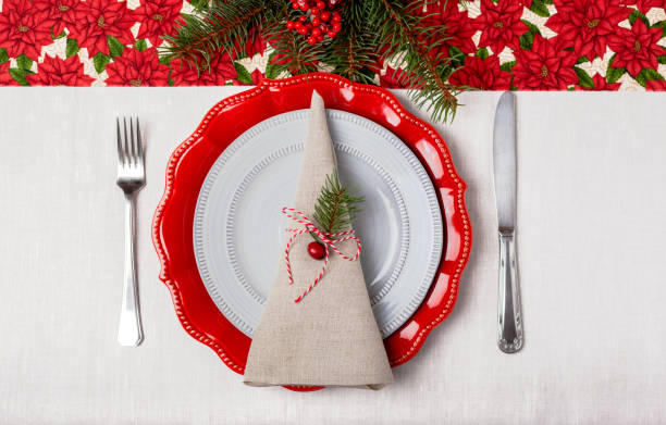 istock Simple table setting of a red and grey plates on a white tablecloth with poinsettia pattern top view 1360072507