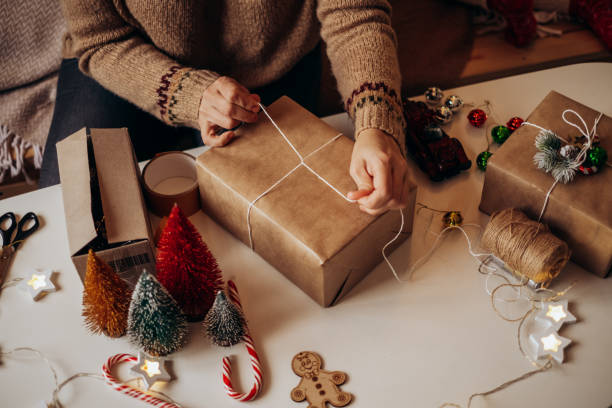 istock Woman s hands wrapping Christmas gift boxes, close up. Unprepared presents on white table with decor elements and items Christmas or New year DIY packing Concept. 1360073351