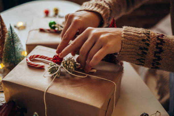 istock Woman s hands wrapping Christmas gift boxes, close up. Unprepared presents on white table with decor elements and items Christmas or New year DIY packing Concept. 1360073381