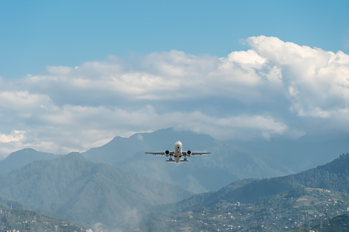 Passenger plane took off from the airport near the mountains. Plane flies against the background of the sky with clouds, mountains, private houses. Travel