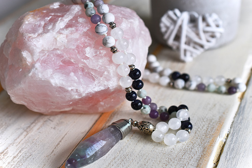 A close up image of a raw rose quartz crystal with fluorite meditation mala necklace.