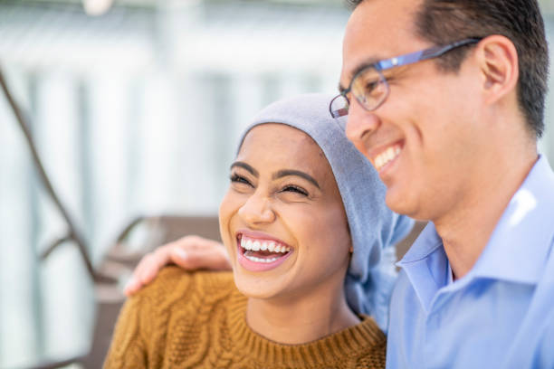 Cancer Patient Sitting Outside with Her Father A young woman battling Cancer is embraced by her Father as they sit outside enjoying the sunshine.  The young woman is dressed casually and has a head scarf on while her Father hugs her from the side.  Both are smiling as they enjoy the close moment together. canada close up color image day stock pictures, royalty-free photos & images