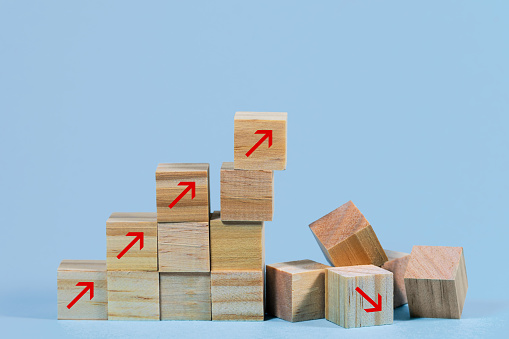 Collapsed stair structure of wooden cubes with upward pointing arrows, business risk due to inflation, global crisis, supply shortage or unsustainable financial concept, light blue background with copy space