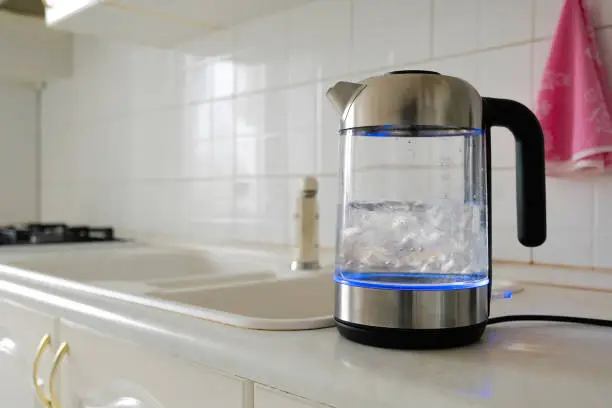 Glass electric kettle boils on the kitchen table. Modern household appliances