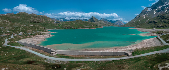 Reservoir wall at the reservoir lake Lago Bianco at the Bernina Pass with blue sky and sun from above in summer