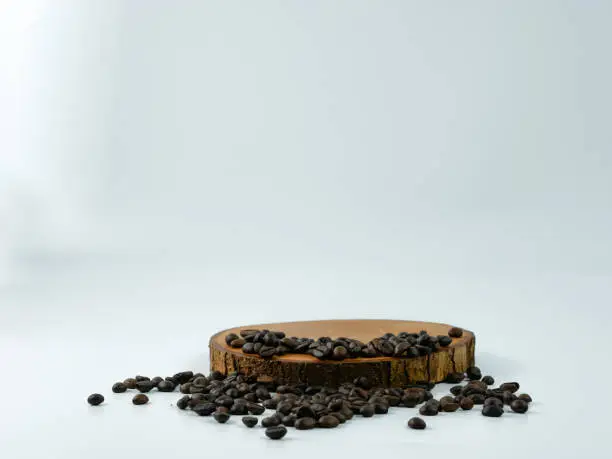 Coffee beans scattered on a round wooden plank isolated on a white background. Product placement concept.
