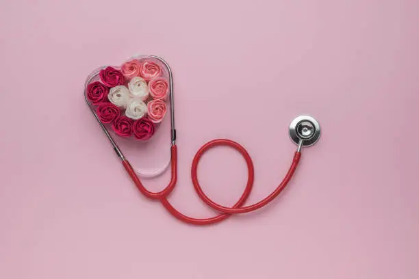A red stethoscope and a heart made of rosebuds. The concept of medical examination. Flat lay.