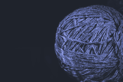 A ball of yarn on a black background. Material for knitting. Home crafts and hobbies. Colored in trendy color of year 2022 Very Peri. Selective focus, copy space