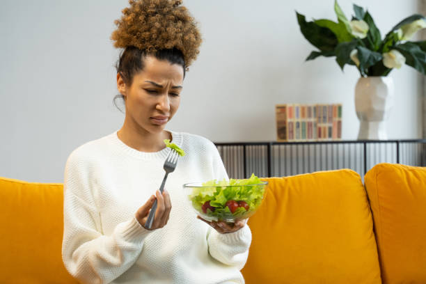 la femme noire n’aime pas manger de la salade de légumes, des aliments sains, assise sur le canapé - black hair photos et images de collection