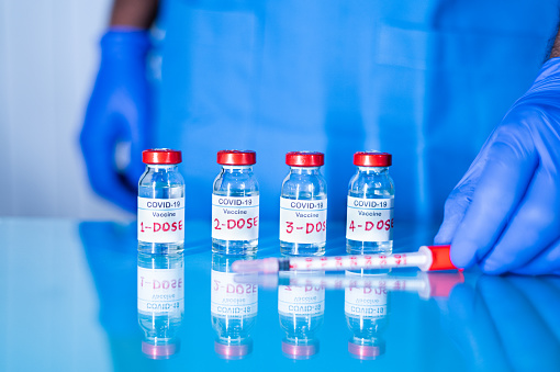 Close up of doctor placing multiple doses of covid-19 or coronavirus vaccine and syringe on table for vaccination to protect against coronavirus variants or to stop pandemic.