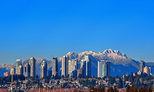 New residential area of  high-rise buildings in the city of Burnaby, construction site in the center of the city against the backdrop of snow covered mountain range and blue sky