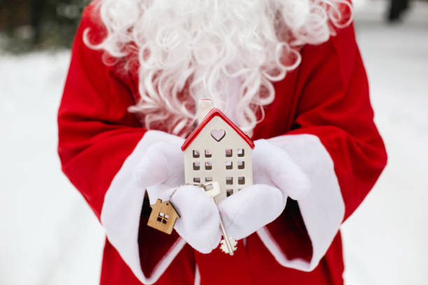 House key with keychain cottage in hands of Santa Claus outdoor in snow. Deal for real estate, purchase, construction, relocation, mortgage. Cozy home. Merry Christmas, new year booking event and hall stock photo