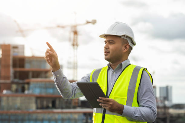 istock Asian engineer handsome man or architect use tablet with white safety helmet in city construction site . Standing on rooftop building construction at capital. 1360128646