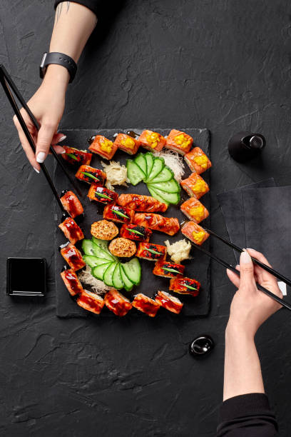 Two female hands using chopsticks to take rolls from sushi set stock photo