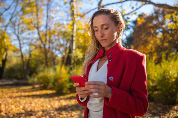 istock Elegant woman using smart phone in the forest in autumn 1360131400