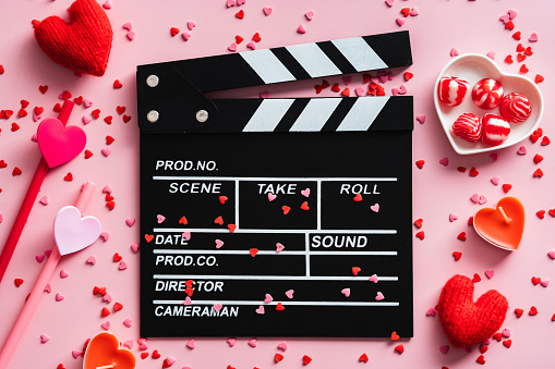 Clapper board and Valentines Day decorations on pink table. Overhead view.