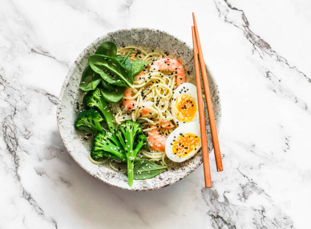 istock Ramen noodles with shrimp, broccoli, spinach and boiled egg on a light background, top view 1360134591