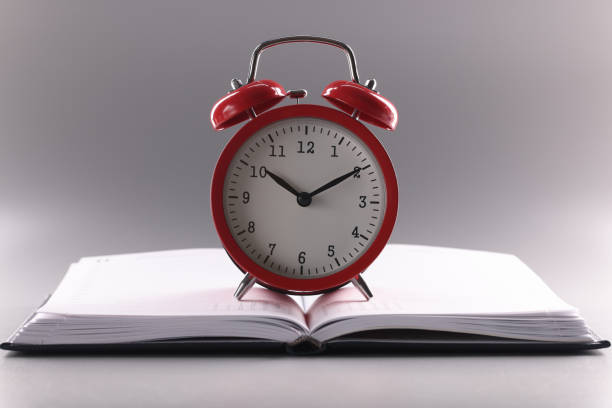 istock Red retro clock stand on top of open notebook or book 1360139158