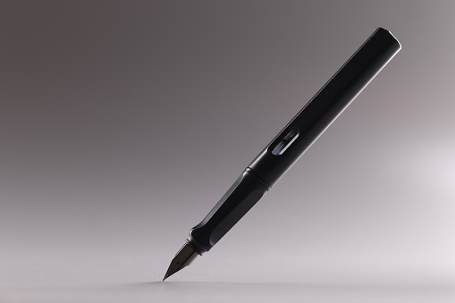 Close-up of black feather pen, sharp tip, tool for writing, refill ink container. Pen in grey background. Stationery, writing equipment, office concept