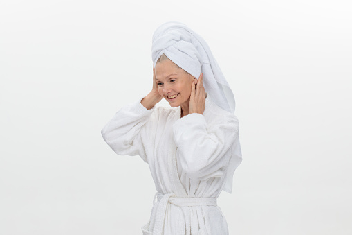 Close-up of a mature woman in a white bathrobe with a towel on her head applies isolated on white background