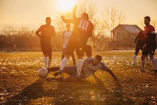 Group of people, male soccer players playing a match on a soccer field on winter day outdoors. Player performing a tackle