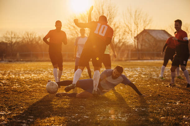 Male soccer match Group of people, male soccer players playing a match on a soccer field on winter day outdoors. Player performing a tackle foul stock pictures, royalty-free photos & images